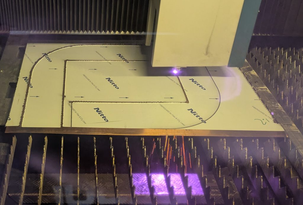 Laser cutting copper sheet with protective film, producing custom curved profiles for Kraft Metals.