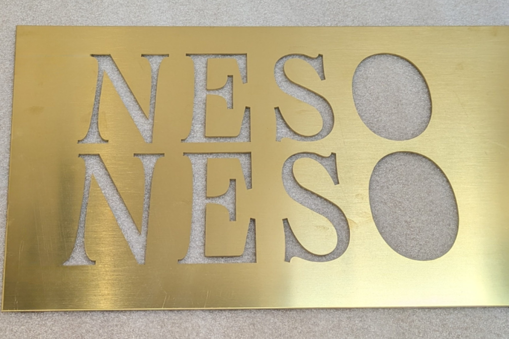 Laser cut brass panel with letter and oval cut-outs.